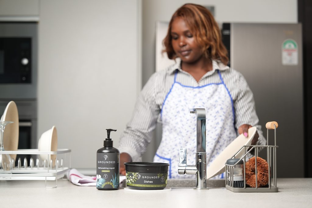 Image of a lady cleaning a plate with Grounded and Vituzote cleaning products in Kenya.